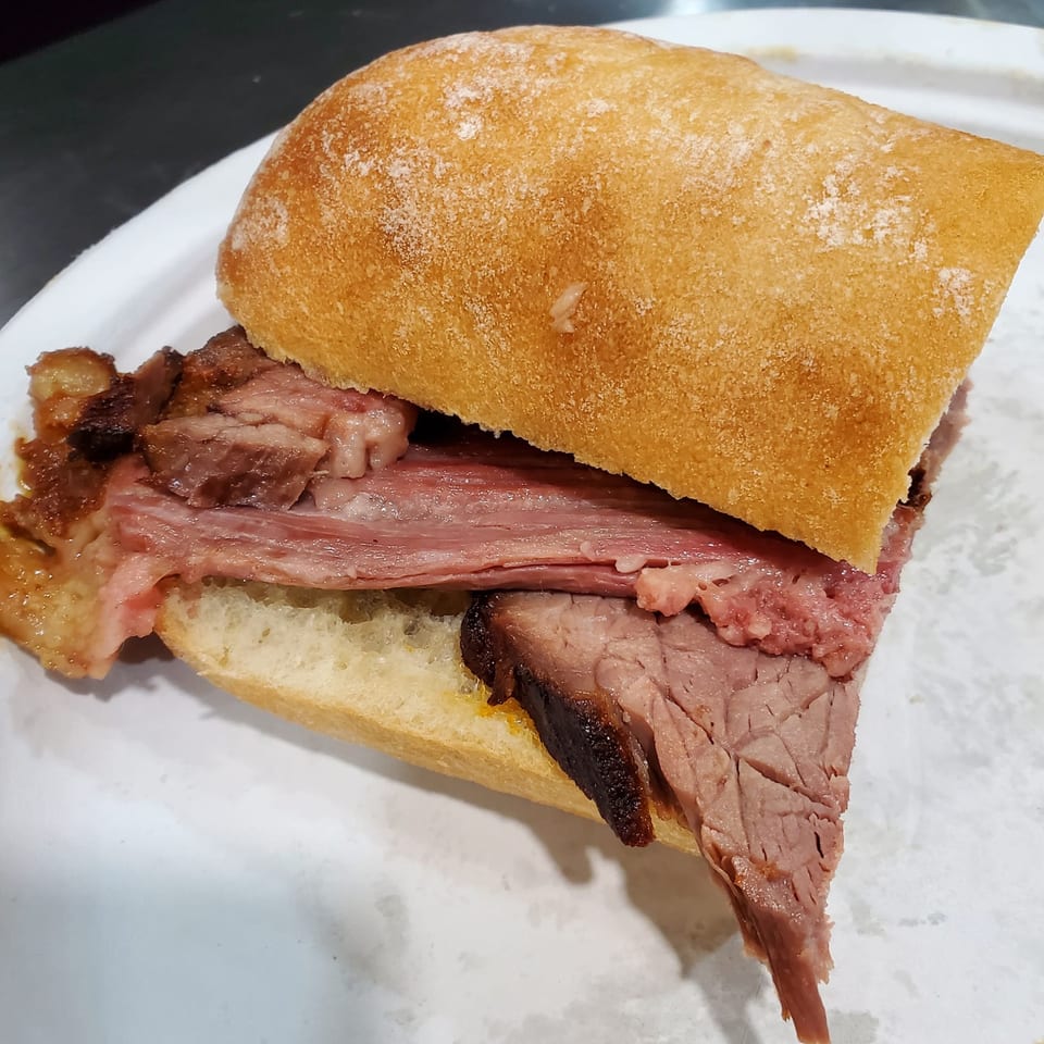 Close-up of a brisket sandwich with thick slices of meat on a white bun.