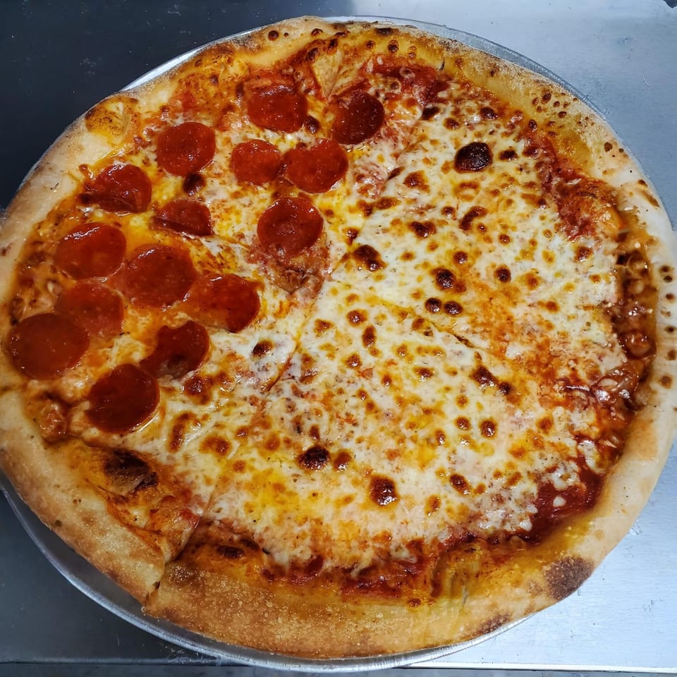 A large, half-pepperoni, half-cheese pizza from Eastside Market LLC on a metal pan.